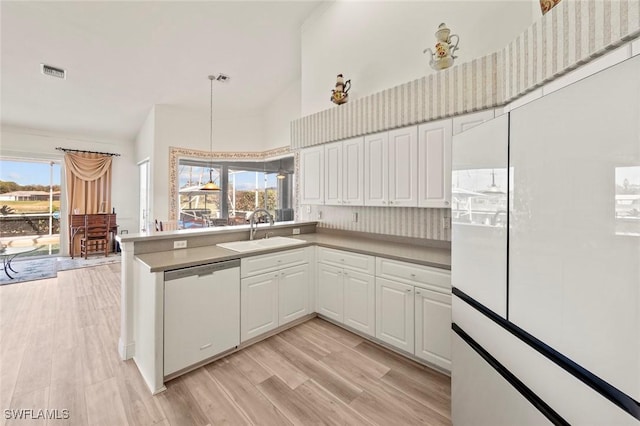 kitchen featuring visible vents, dishwashing machine, light wood-style floors, white cabinetry, and a sink