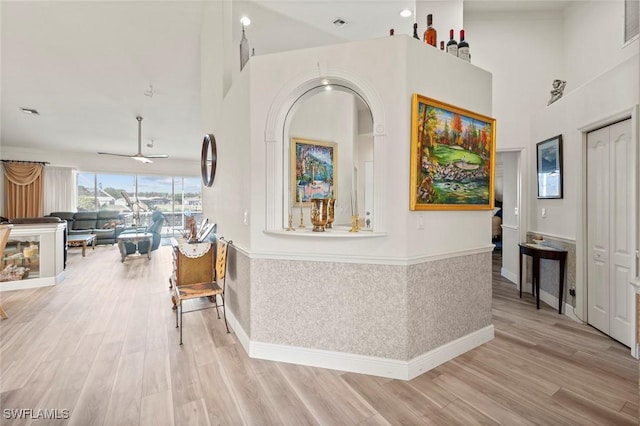 corridor featuring a towering ceiling, visible vents, wood finished floors, and wainscoting