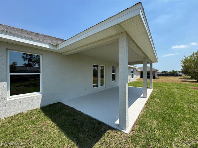 back of house with a lawn, stucco siding, a patio area, and roof with shingles