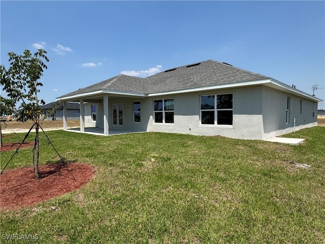 rear view of house featuring a lawn, stucco siding, a patio area, and roof with shingles