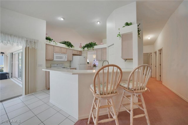 kitchen featuring light tile patterned floors, white appliances, a breakfast bar, light brown cabinetry, and kitchen peninsula