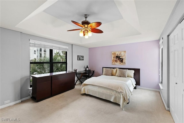 carpeted bedroom with ceiling fan, a raised ceiling, and a closet