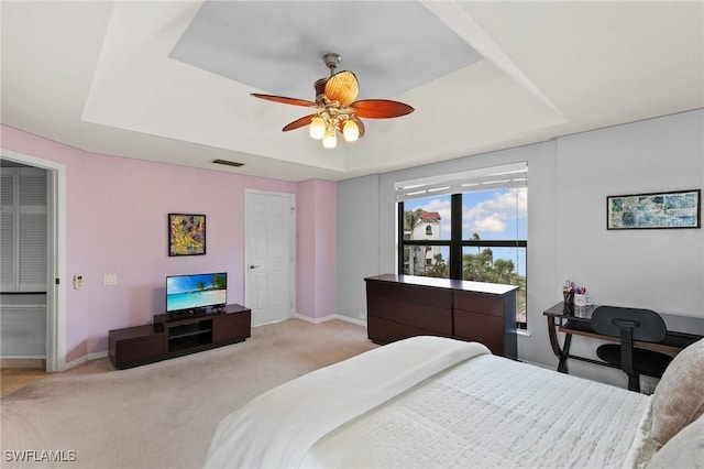 bedroom featuring light carpet, ceiling fan, and a tray ceiling