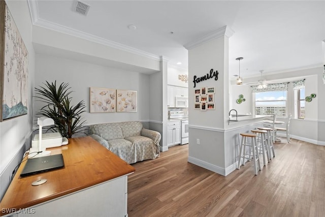 living room with sink, ornamental molding, ceiling fan, and light wood-type flooring