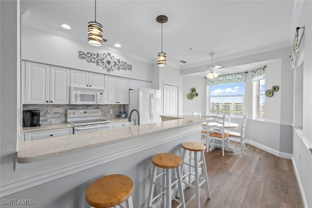 kitchen with a kitchen bar, white cabinetry, white appliances, light stone countertops, and decorative backsplash