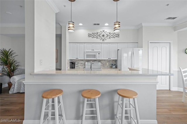 kitchen featuring a breakfast bar, kitchen peninsula, white appliances, decorative backsplash, and white cabinets