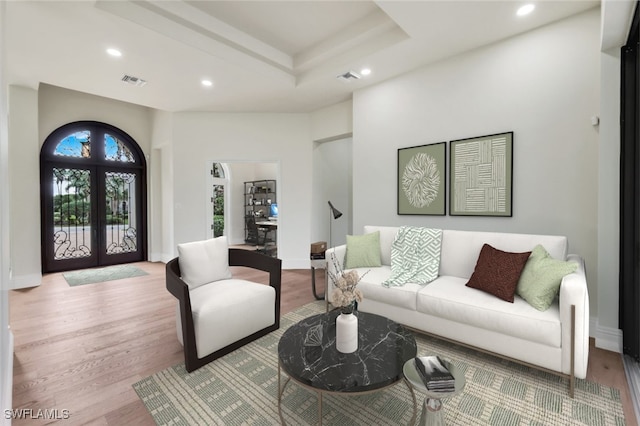 living room featuring french doors, a raised ceiling, a high ceiling, and light wood-type flooring