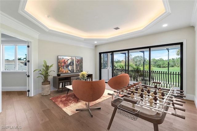 living area with a raised ceiling, wood-type flooring, plenty of natural light, and ornamental molding