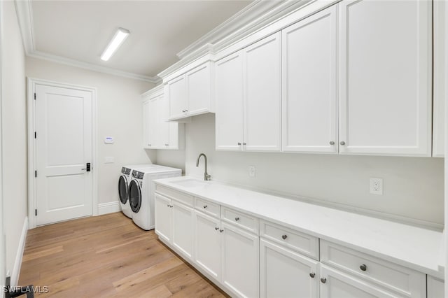 clothes washing area featuring washing machine and clothes dryer, sink, cabinets, ornamental molding, and light hardwood / wood-style floors