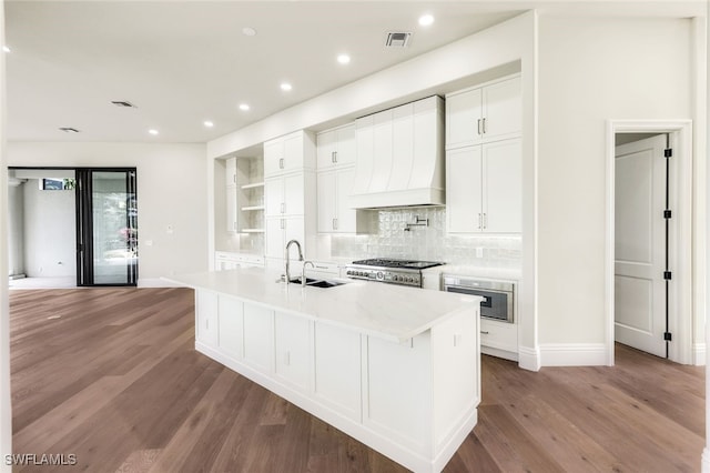 kitchen featuring white cabinetry, sink, light hardwood / wood-style floors, custom range hood, and a center island with sink