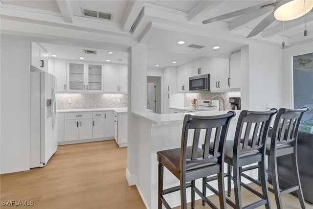 kitchen featuring a breakfast bar, white cabinetry, range with electric stovetop, white fridge with ice dispenser, and kitchen peninsula