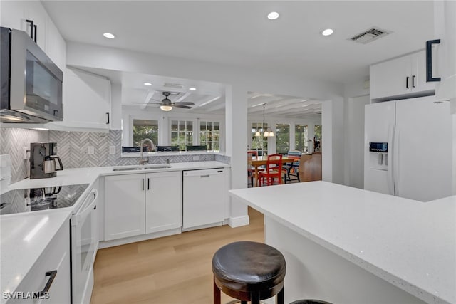 kitchen with white cabinetry, white appliances, a breakfast bar, and sink