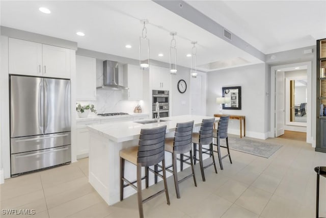 kitchen with wall chimney exhaust hood, a breakfast bar area, a center island with sink, stainless steel appliances, and white cabinets