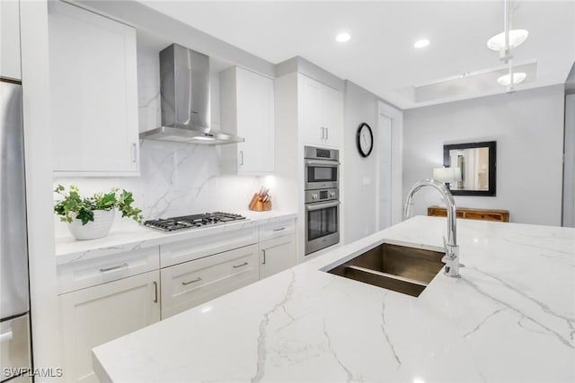 kitchen featuring white cabinetry, light stone countertops, sink, and wall chimney range hood