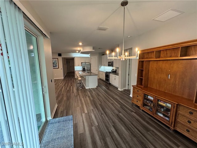 interior space with white cabinets, a kitchen bar, hanging light fixtures, stainless steel appliances, and a center island with sink