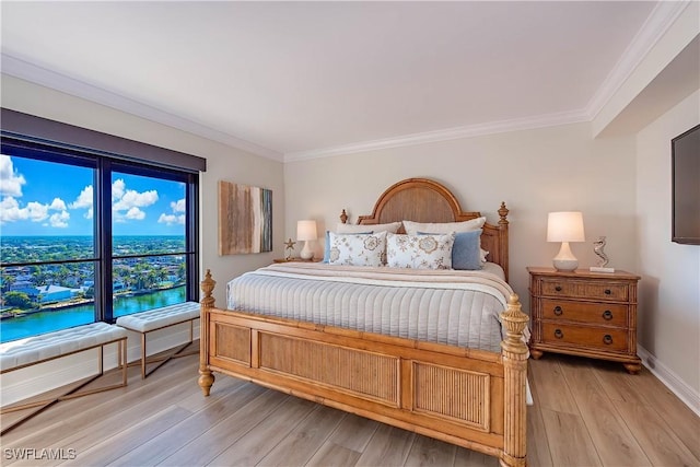 bedroom with a water view, light wood finished floors, baseboards, and ornamental molding