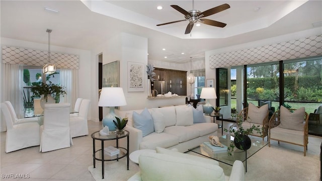 tiled living room with ceiling fan and a tray ceiling