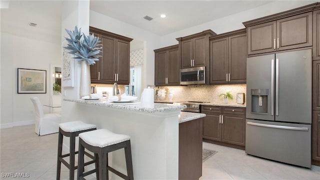 kitchen with dark brown cabinetry, light stone counters, and appliances with stainless steel finishes