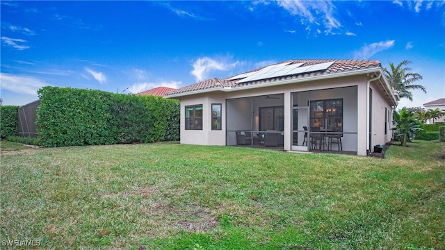 back of property featuring a sunroom, a lawn, and solar panels