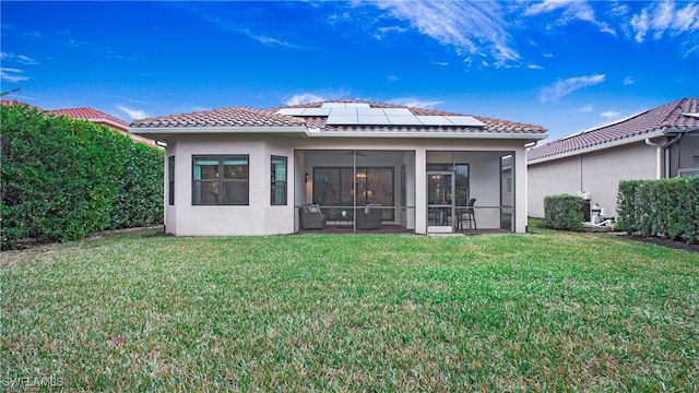 back of property featuring a sunroom, a yard, and solar panels