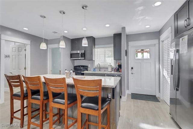 kitchen with pendant lighting, stainless steel appliances, light stone countertops, an island with sink, and a kitchen bar