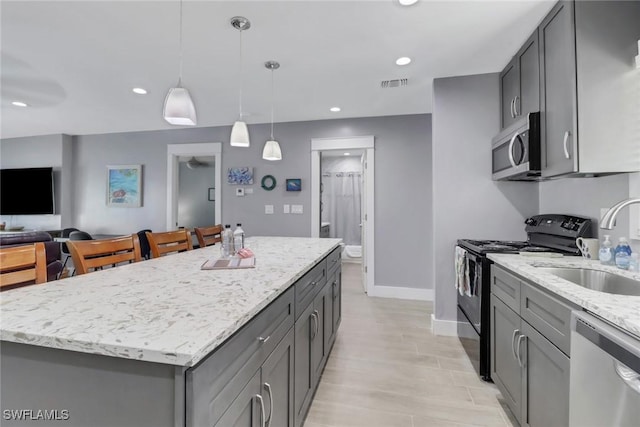 kitchen with appliances with stainless steel finishes, pendant lighting, gray cabinetry, a center island, and light stone counters