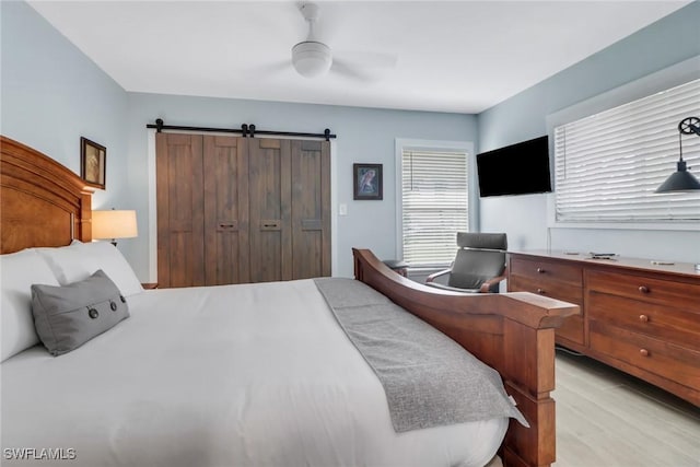 bedroom featuring light hardwood / wood-style floors, a barn door, ceiling fan, and a closet