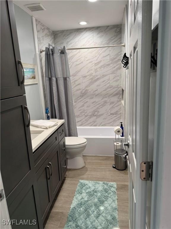 full bathroom featuring vanity, hardwood / wood-style floors, shower / bathtub combination with curtain, and toilet