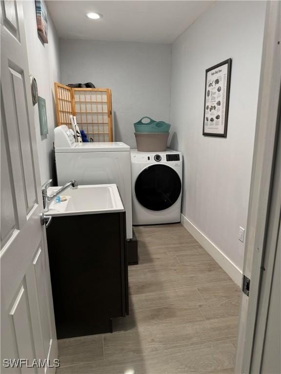 clothes washing area with washing machine and dryer, sink, and light hardwood / wood-style floors