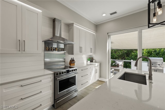 kitchen with stainless steel electric range oven, sink, hanging light fixtures, light stone countertops, and wall chimney range hood