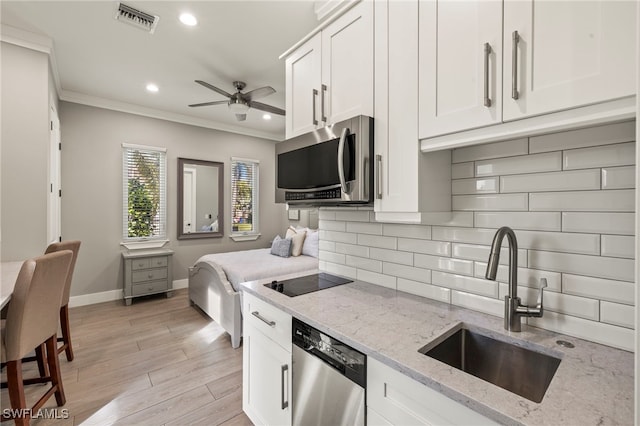 kitchen with sink, white cabinetry, ornamental molding, stainless steel appliances, and light stone countertops