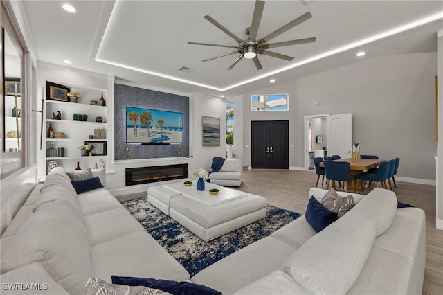 living room featuring a tray ceiling, built in features, ceiling fan, and light wood-type flooring