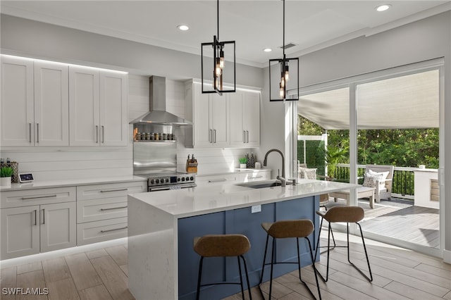 kitchen featuring wall chimney range hood, sink, white cabinets, and a center island with sink