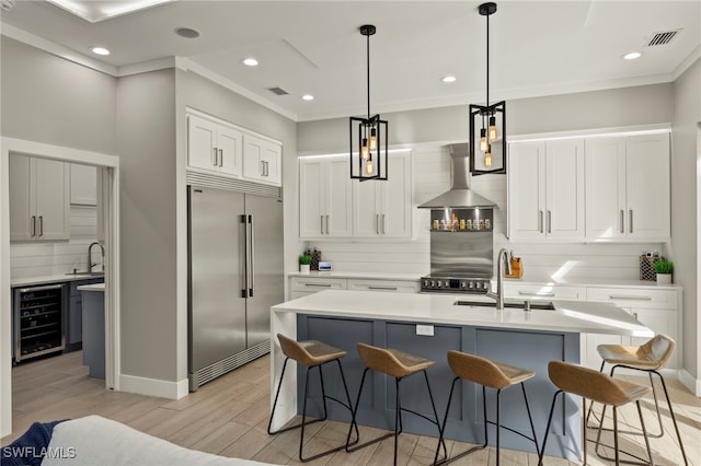 kitchen featuring wine cooler, sink, a center island with sink, appliances with stainless steel finishes, and wall chimney range hood