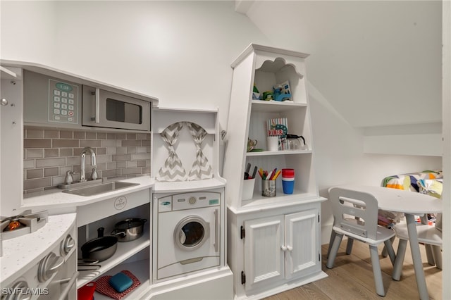 clothes washing area with washer / clothes dryer, sink, and light wood-type flooring