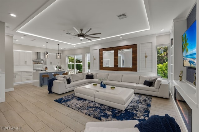 living room with ceiling fan, sink, a raised ceiling, and light hardwood / wood-style floors