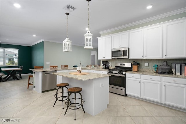 kitchen with a breakfast bar, appliances with stainless steel finishes, white cabinetry, hanging light fixtures, and a kitchen island