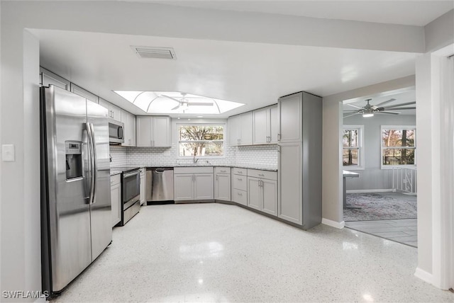 kitchen featuring gray cabinets, appliances with stainless steel finishes, plenty of natural light, and a skylight