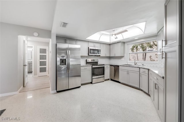 kitchen with tasteful backsplash, stainless steel appliances, gray cabinets, and sink