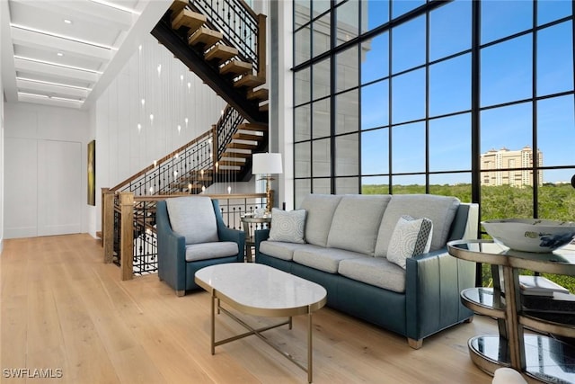 living room with beamed ceiling, a towering ceiling, floor to ceiling windows, and light wood-type flooring