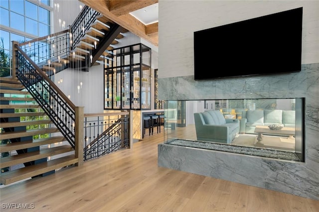 staircase with a fireplace, beam ceiling, wood-type flooring, and a high ceiling