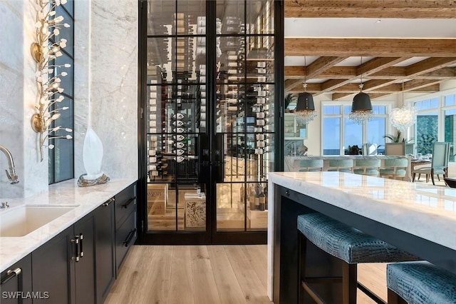 bar with decorative light fixtures, sink, beam ceiling, light stone counters, and light wood-type flooring