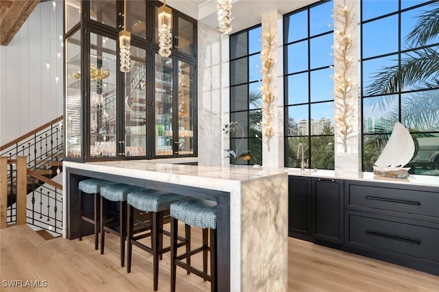 bar featuring light stone counters, decorative light fixtures, and light hardwood / wood-style floors