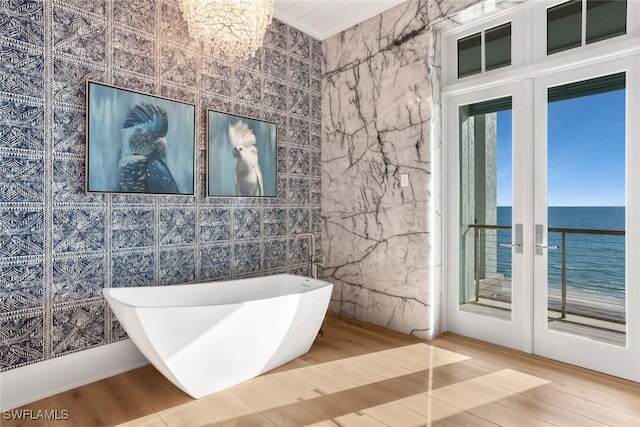 bathroom featuring a water view, wood-type flooring, french doors, and a tub