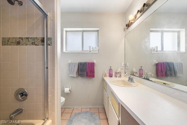 bathroom featuring toilet, bath / shower combo with glass door, vanity, baseboards, and tile patterned floors