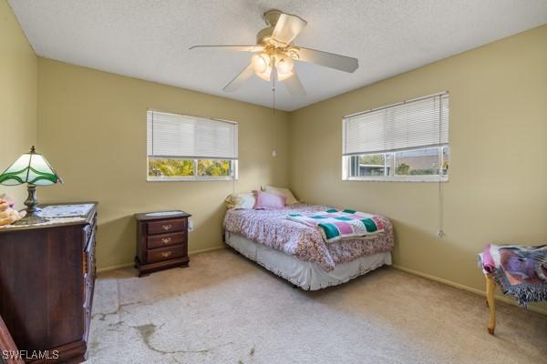 bedroom with ceiling fan, light colored carpet, and a textured ceiling