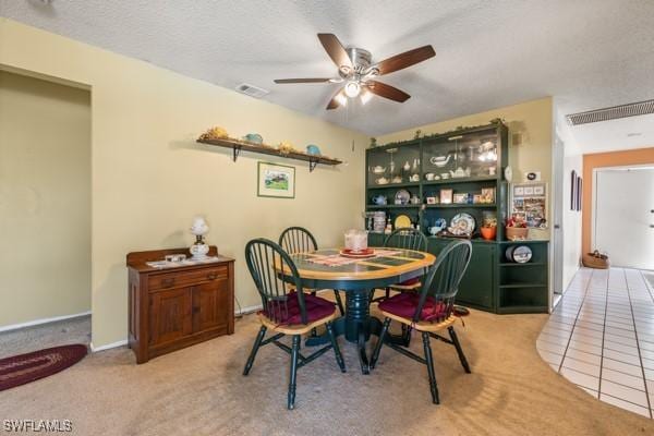 carpeted dining room with a textured ceiling, tile patterned flooring, visible vents, and a ceiling fan