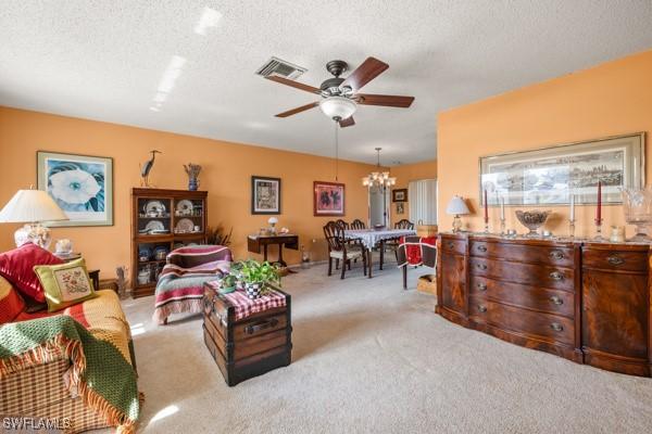 carpeted living room featuring ceiling fan with notable chandelier and a textured ceiling