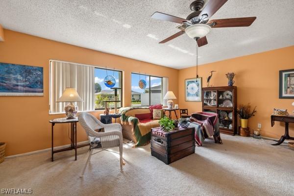 living area featuring ceiling fan, light colored carpet, and a textured ceiling