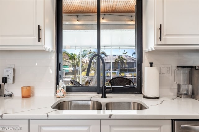 kitchen with white cabinetry, sink, light stone counters, and backsplash